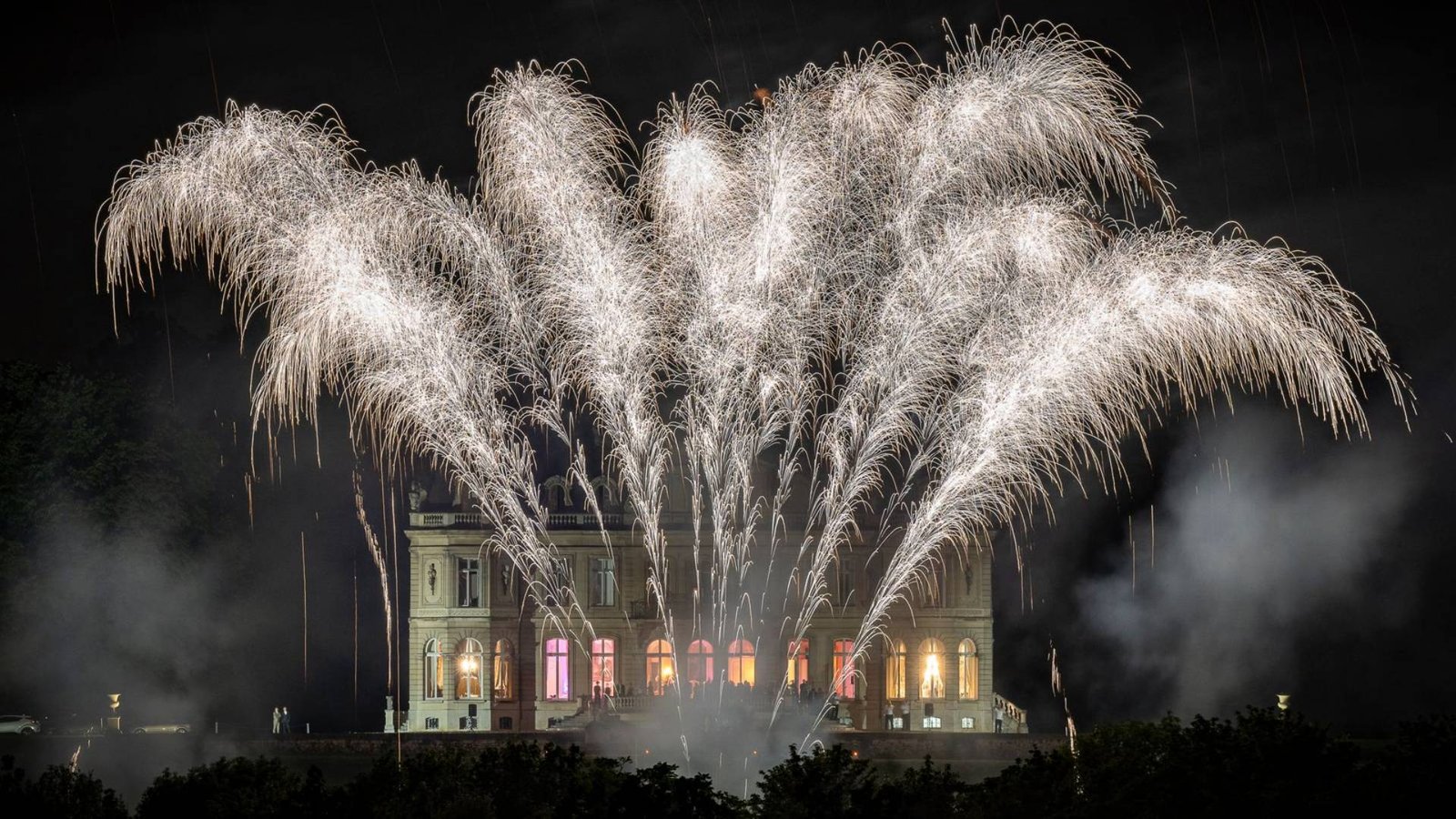 Fireworks displays lighting up the sky above an illuminated building during a Celesta show