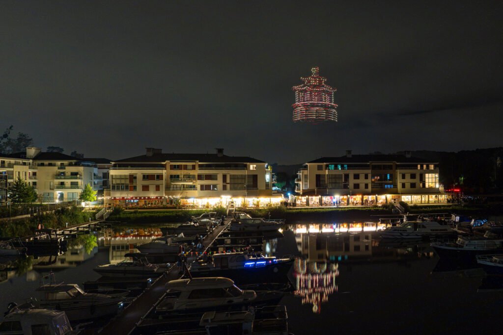 Formation de drones lumineux en rotation au-dessus de la Marina de L’Isle-Adam, reflétée dans le port